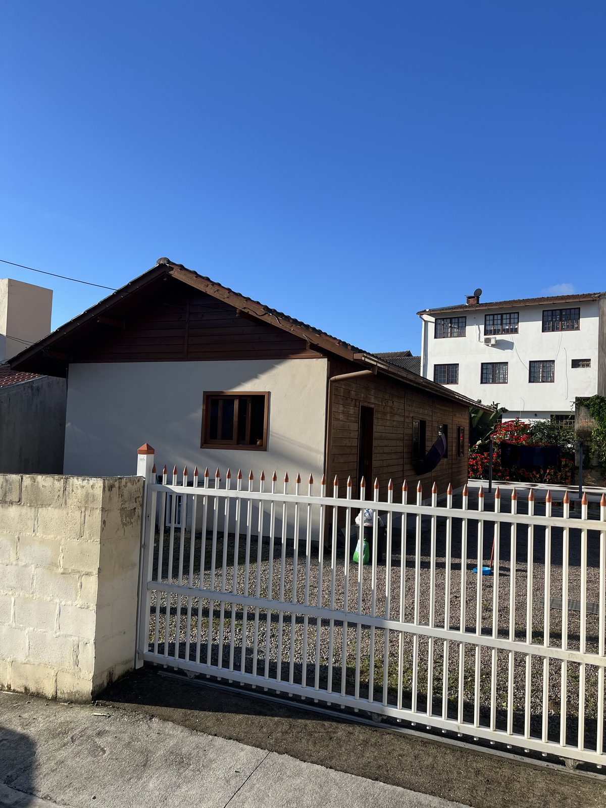 Frente da casa de madeira, com portão e céu azul