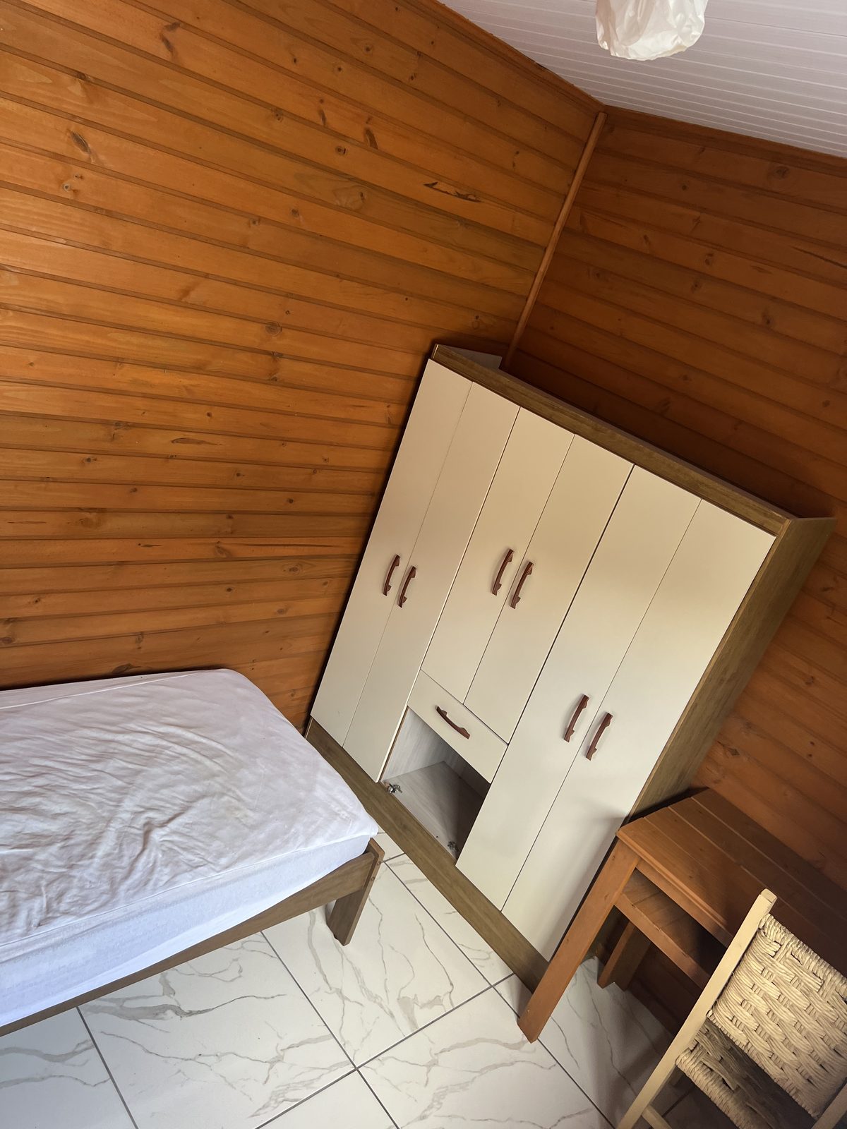 Quarto real com paredes de madeira, cama e luz de fim de tarde